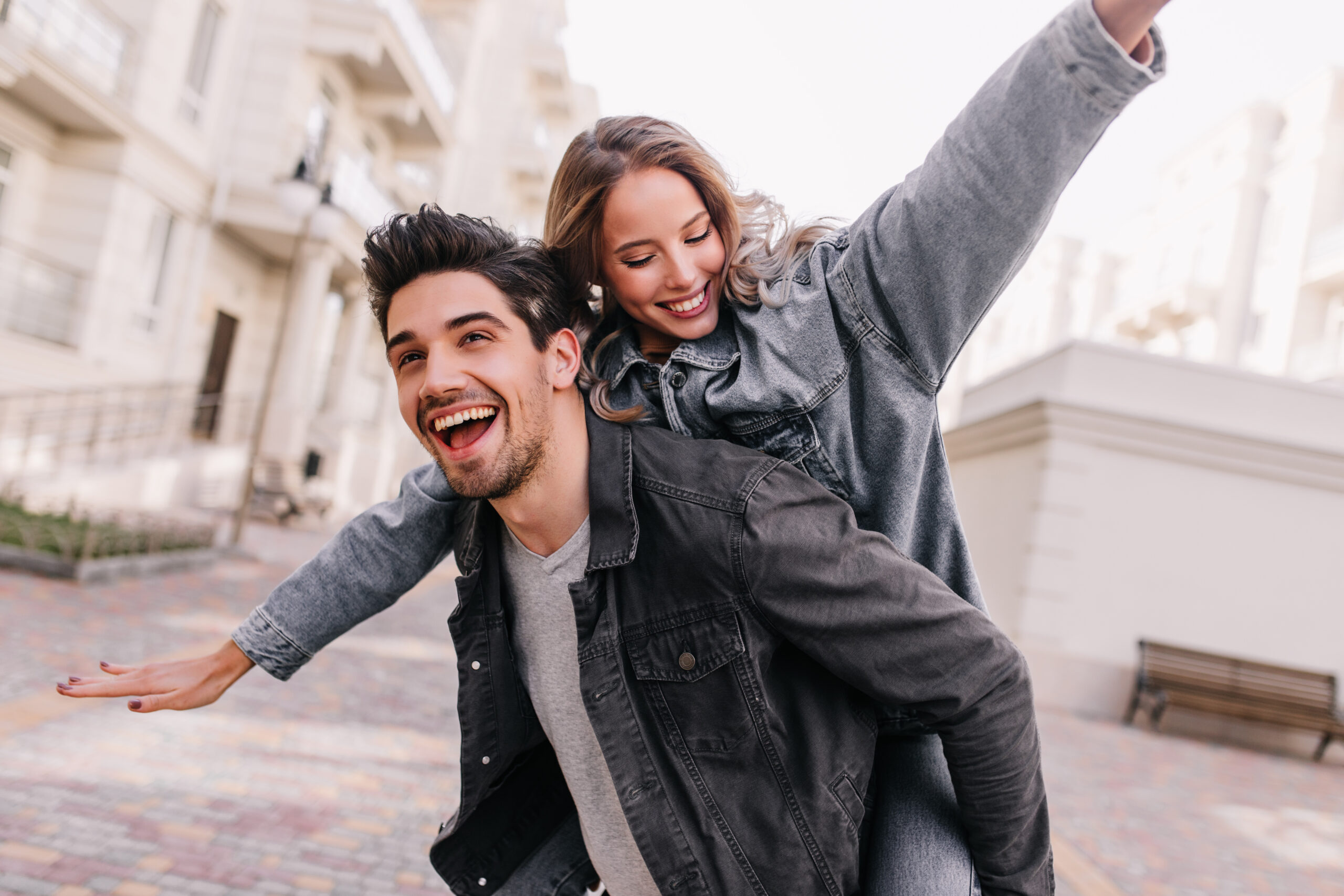 Excited man in black denim jacket chilling with girlfriend. Outdoor photo of happy couple exploring city.